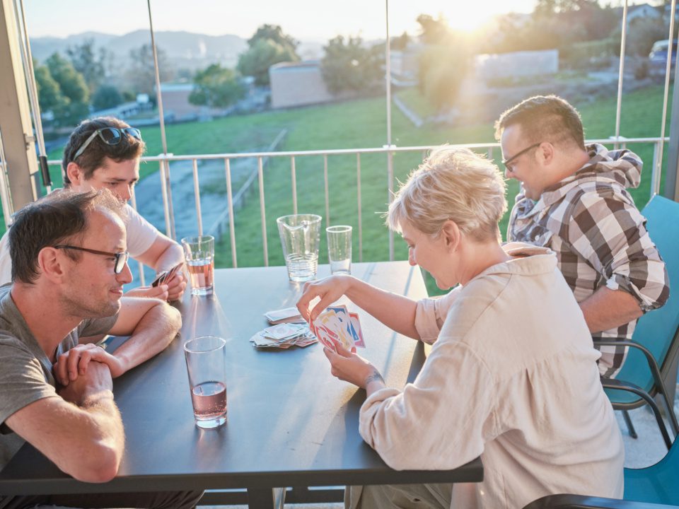 Vier Personen sitzen draussen mit Sirup Getränken am Gartentisch und spielen UNO.